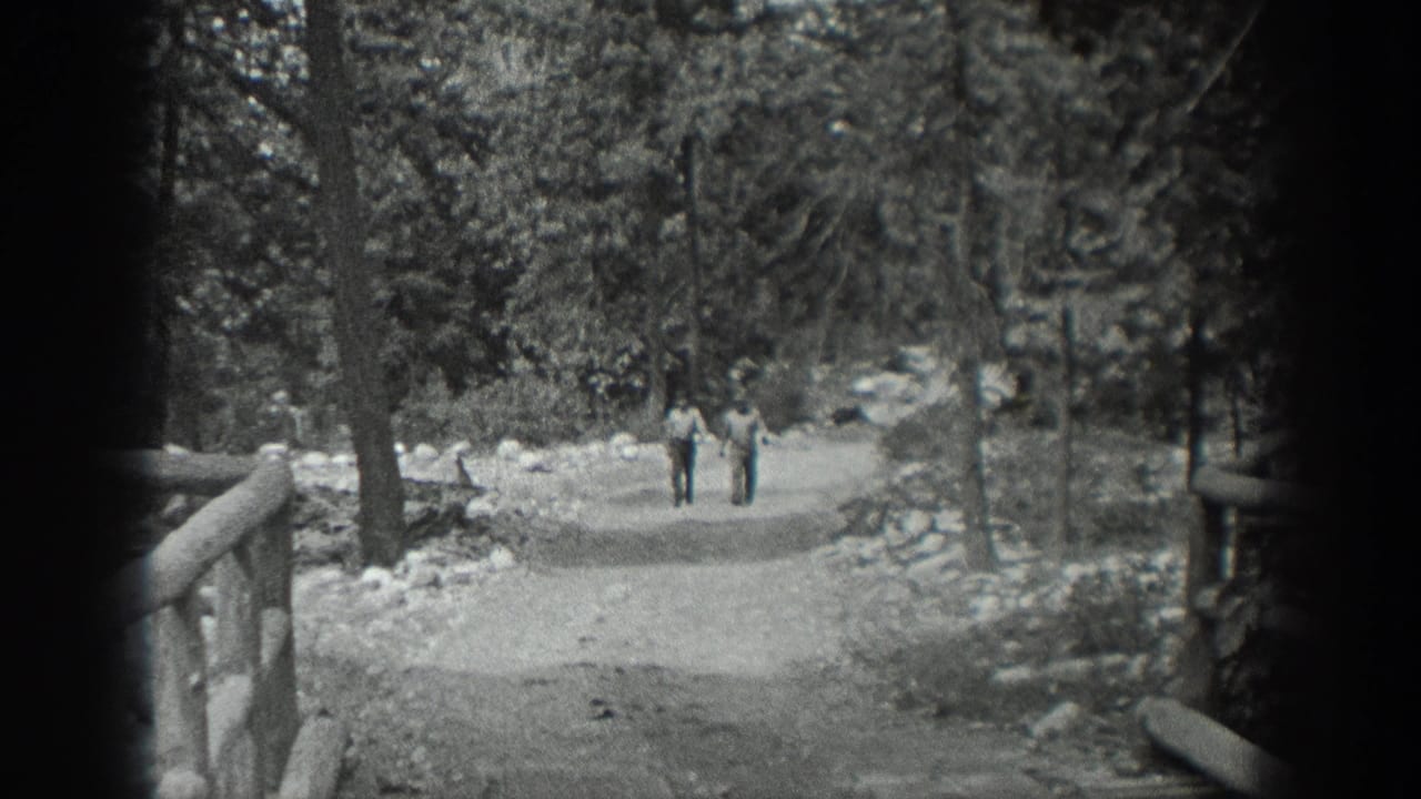 Black-and-white 8mm frame from Washington, 1940, showing two men walking down a wooded dirt trail near a rustic railing.