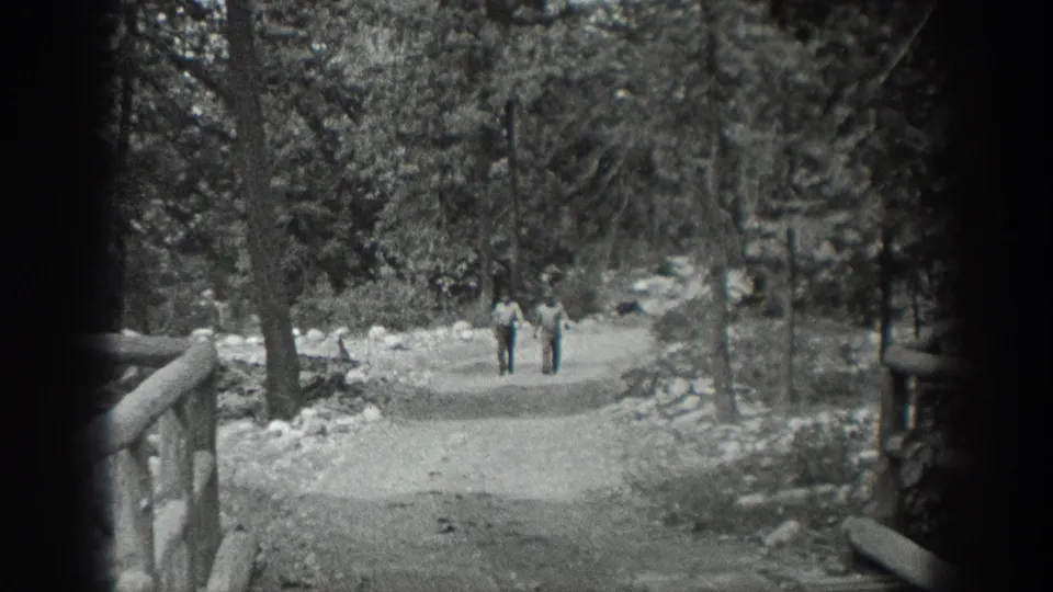 Black-and-white 8mm frame from Washington, 1940, showing two men walking down a wooded dirt trail near a rustic railing.