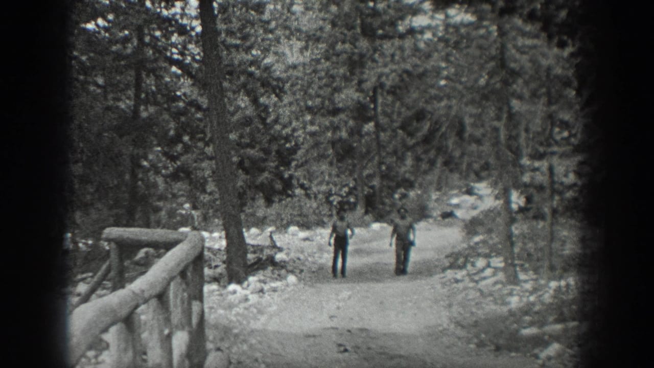 In 1940 Washington home-movie footage, two men appear on a broad dirt path through trees, with a rustic railing in the foreground.