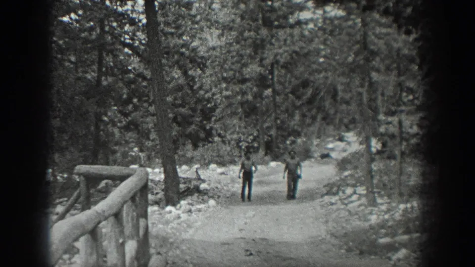 In 1940 Washington home-movie footage, two men appear on a broad dirt path through trees, with a rustic railing in the foreground.