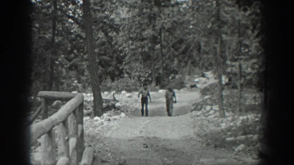 Two men in casual period clothing walk toward the camera on a wide wooded path in Washington, supported by the clip metadata.