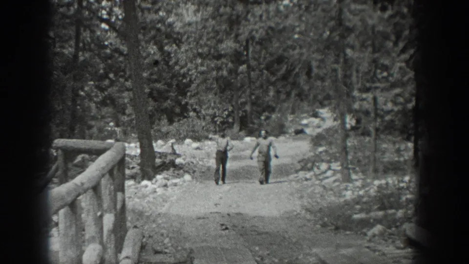 Two men approach on the dirt path, with one lifting an arm in a friendly gesture during the 1940 Washington home-movie scene.