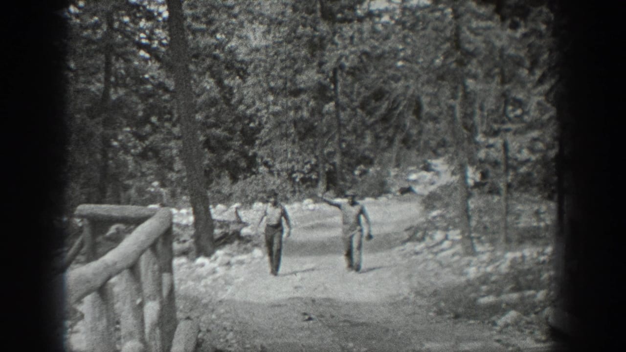 In 1940 Washington home-movie footage, two adult men walk toward the camera on a tree-lined path near a rustic wooden bridge.