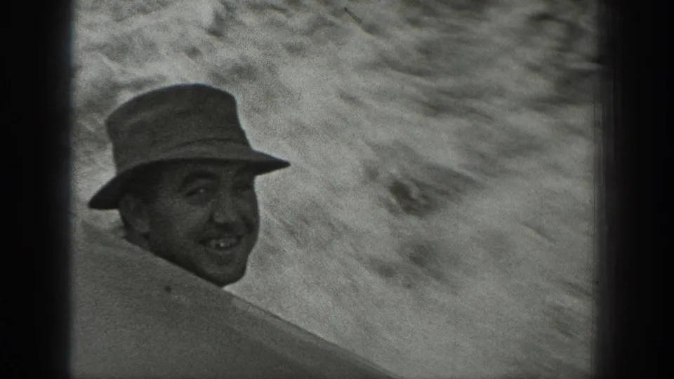 A close, motion-blurred view shows a smiling adult man in a brimmed hat turning toward the 8mm camera.