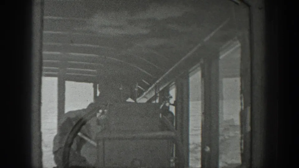 A black-and-white 8mm view looks forward through the boat cabin, showing windows, framing, and passengers during the ride.