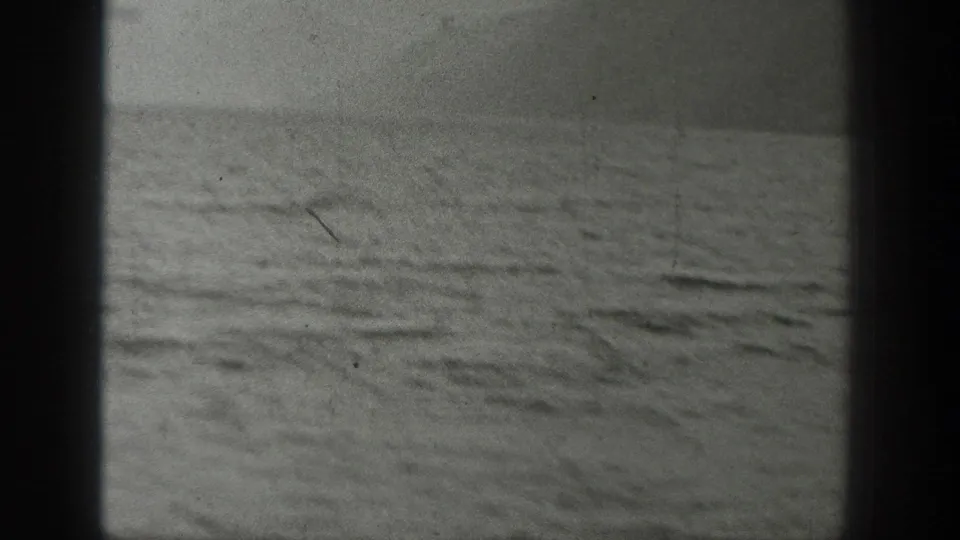 Black-and-white 8mm view of open water from the boat, with soft focus, grain, and dark frame edges.