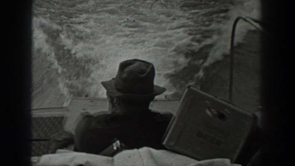 1940 Washington home-movie frame showing a fedora-wearing man seen from behind on a boat, with wake and spray filling the background.