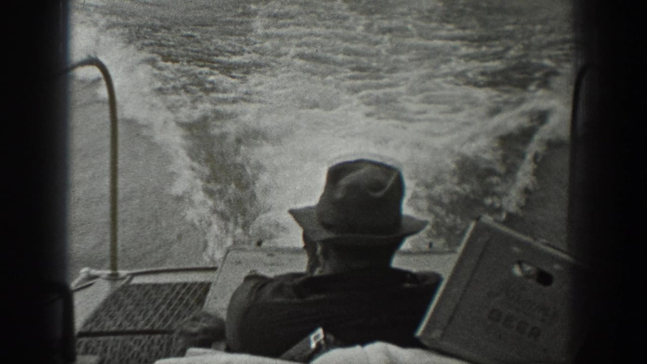 Rear view of a man in a fedora on a boat with foamy water behind him.