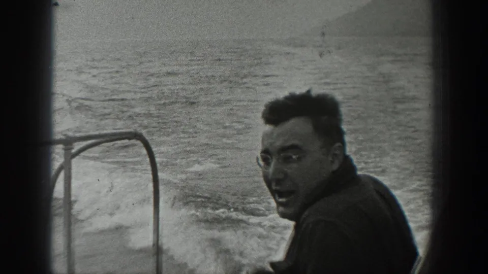 In 1940 Washington home-movie footage, an adult man in glasses smiles back from a motorboat as wake trails behind him.