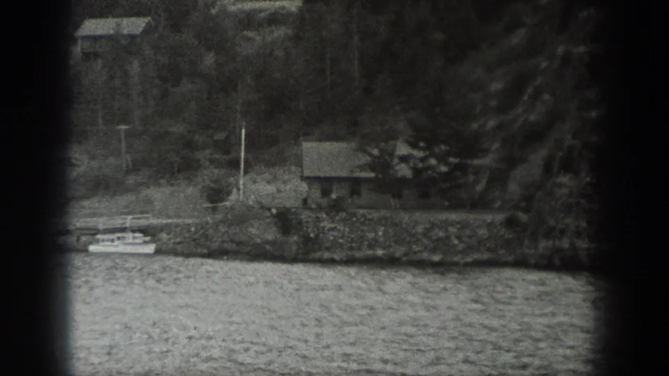 A small shoreline house and wooded bank appear across the water, filmed from the moving boat in Washington home-movie footage.