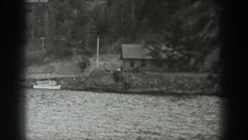 The final frame shows a wooded waterfront with a small house, shoreline stones, and rippled water in black-and-white 8mm texture.