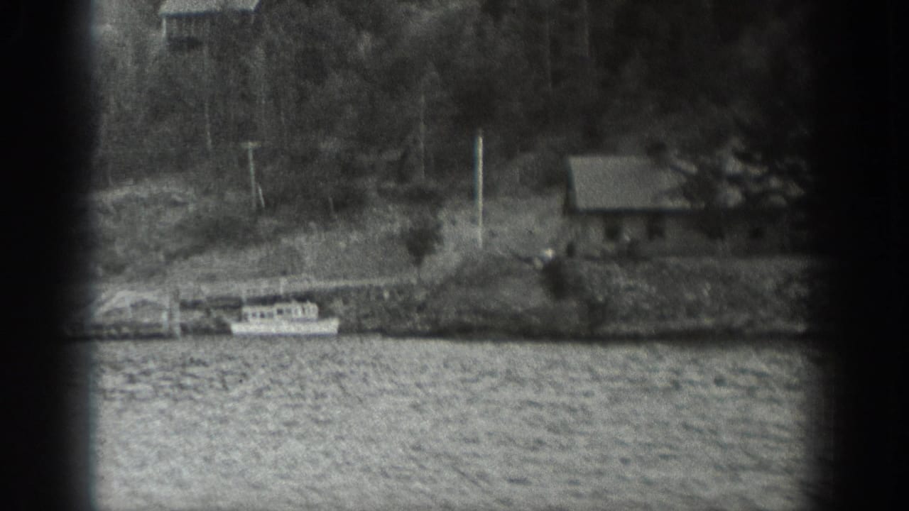 1940 Washington 8mm frame showing small boats at a wooden pier, rippled water, trees, and a small shore building.