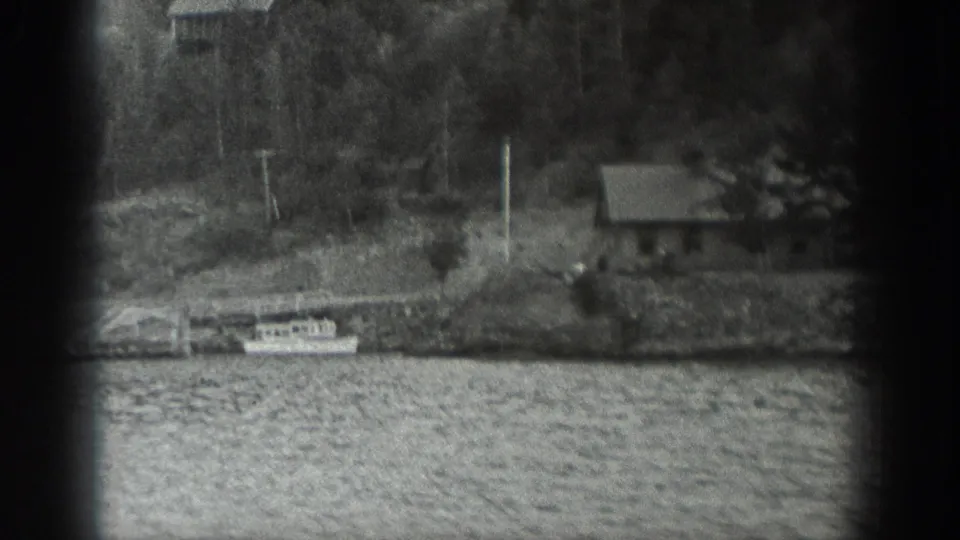 1940 Washington 8mm frame showing small boats at a wooden pier, rippled water, trees, and a small shore building.
