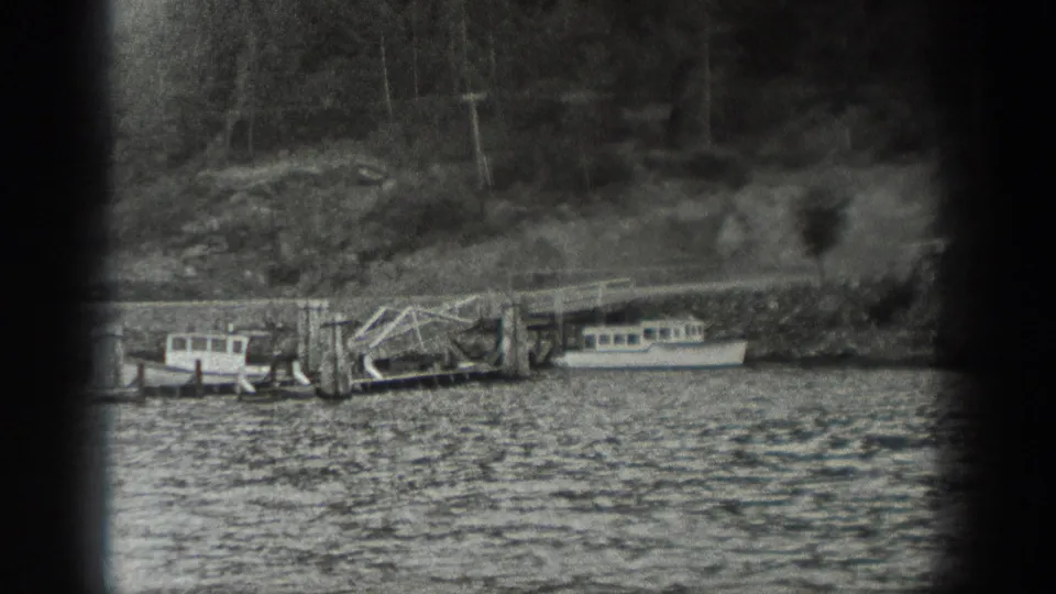 1940 Washington 8mm view of moored boats, a wooden pier, rippled water, a rocky bank, and trees behind the waterfront.
