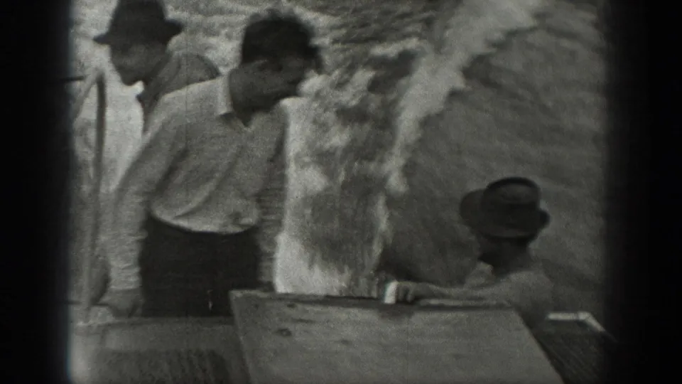 1940 Washington home-movie frame showing three men in period clothing gathered near a boat surface.