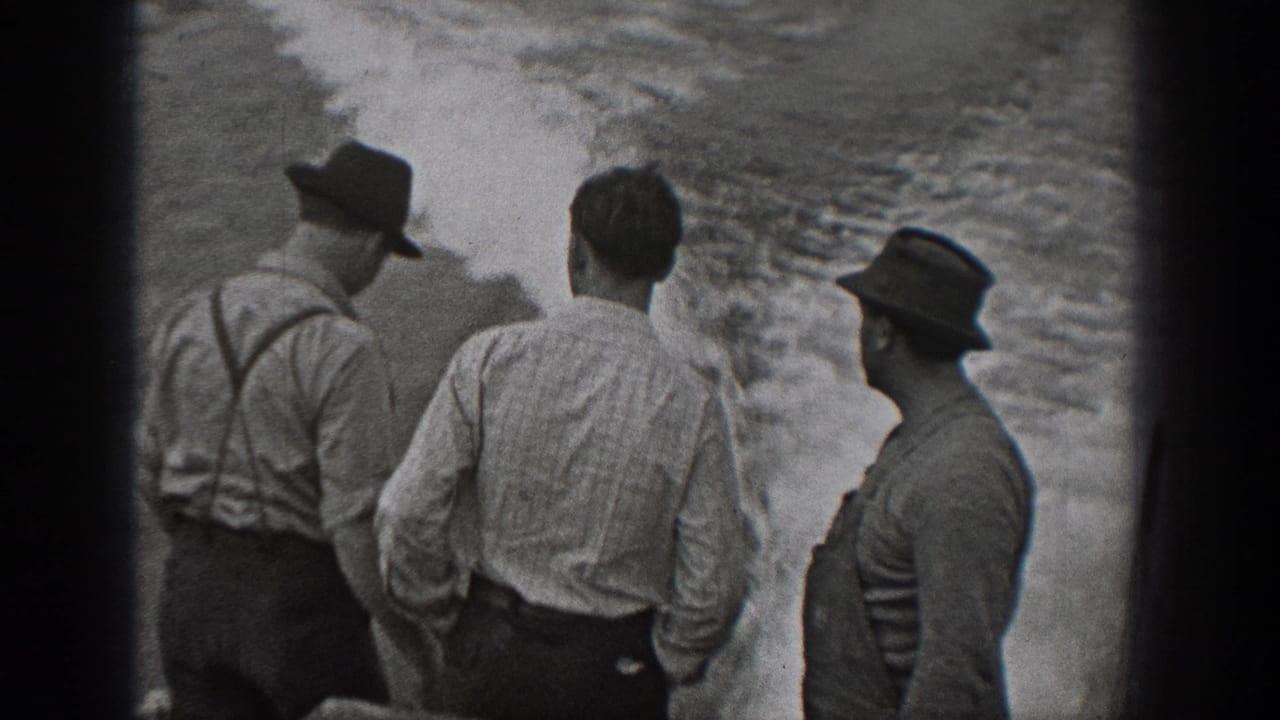 1940 Washington home-movie frame showing adult men in hats, shirts, and suspenders standing on a boat beside churning water.