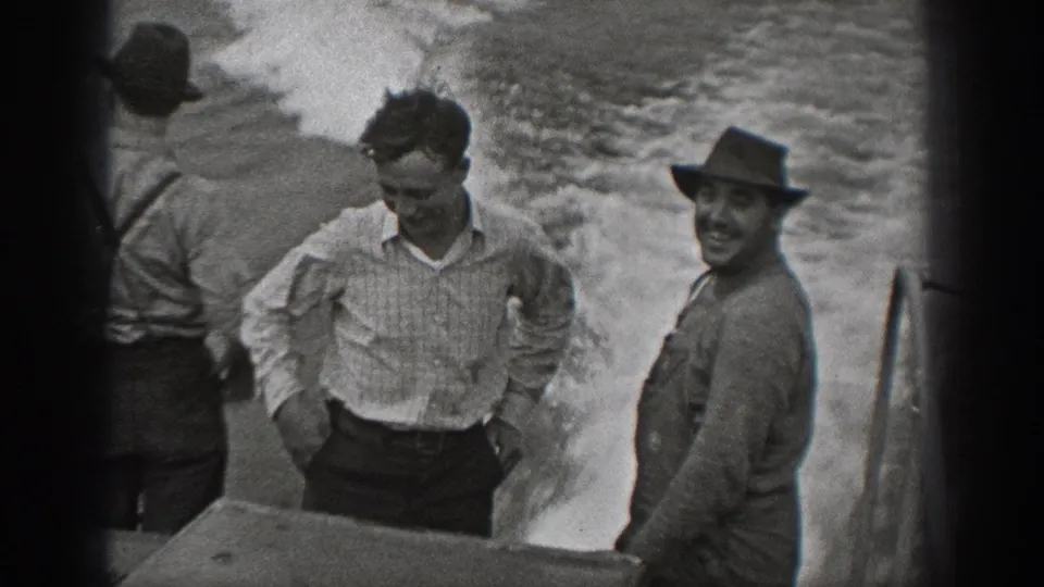 1940 Washington 8mm frame with adult men on a boat, including one smiling toward the camera beside the wake.