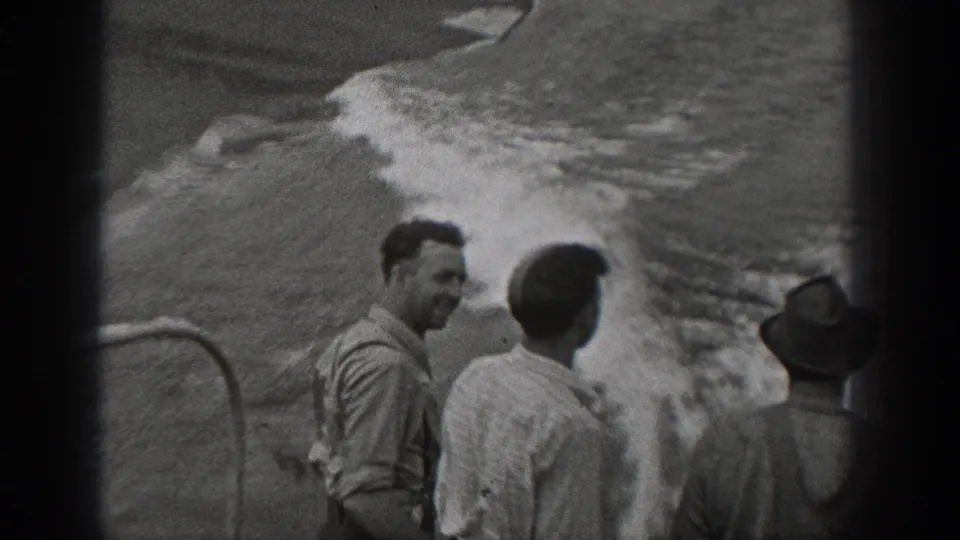 Adult men on a large ship in Washington-area 1940 home-movie footage watch waves breaking alongside the deck.