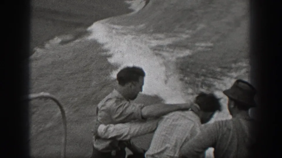 On the ship deck, one adult man extends an arm toward another as passengers face rough water in 1940 home-movie footage.
