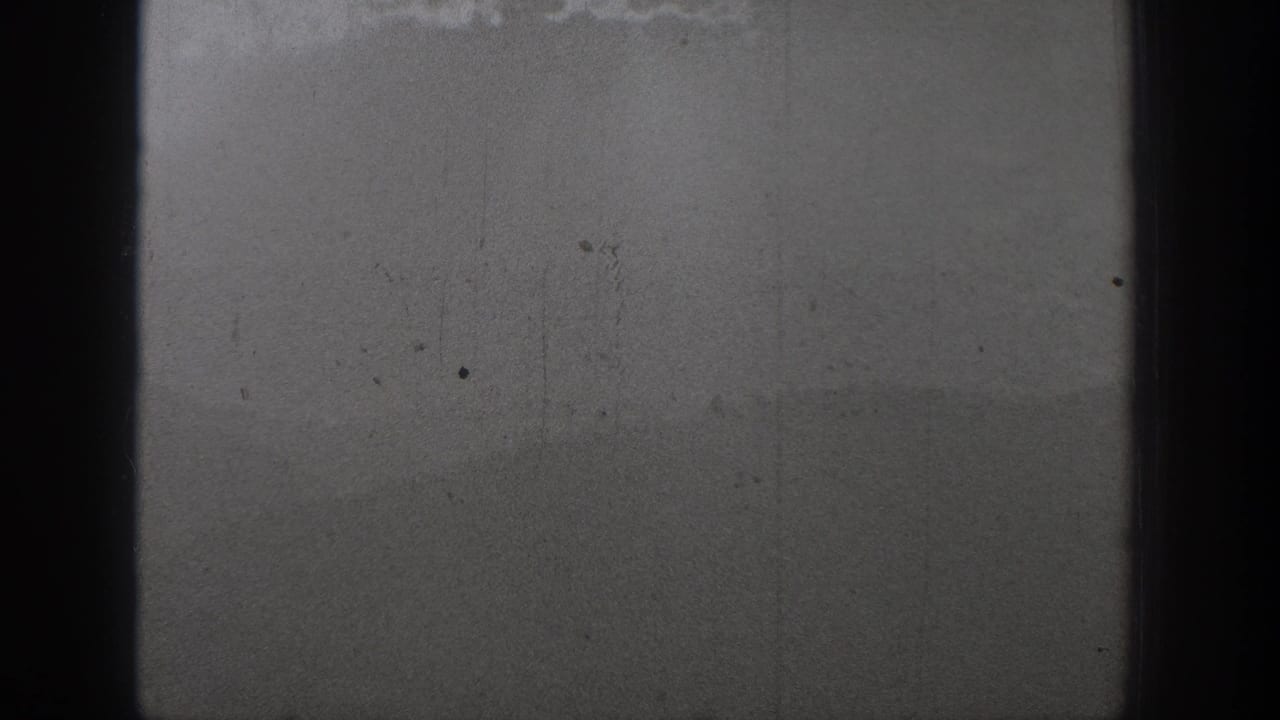 1940 Washington 8mm frame showing distant swimmers in open water below a misty hill or shoreline silhouette.