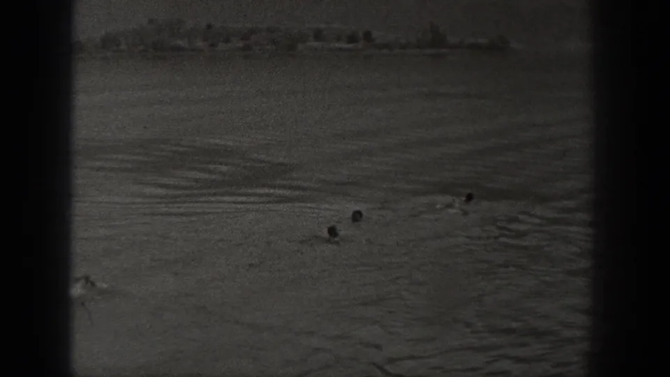 1940 Washington home-movie frame showing distant people in the water and a soft shoreline across the horizon.