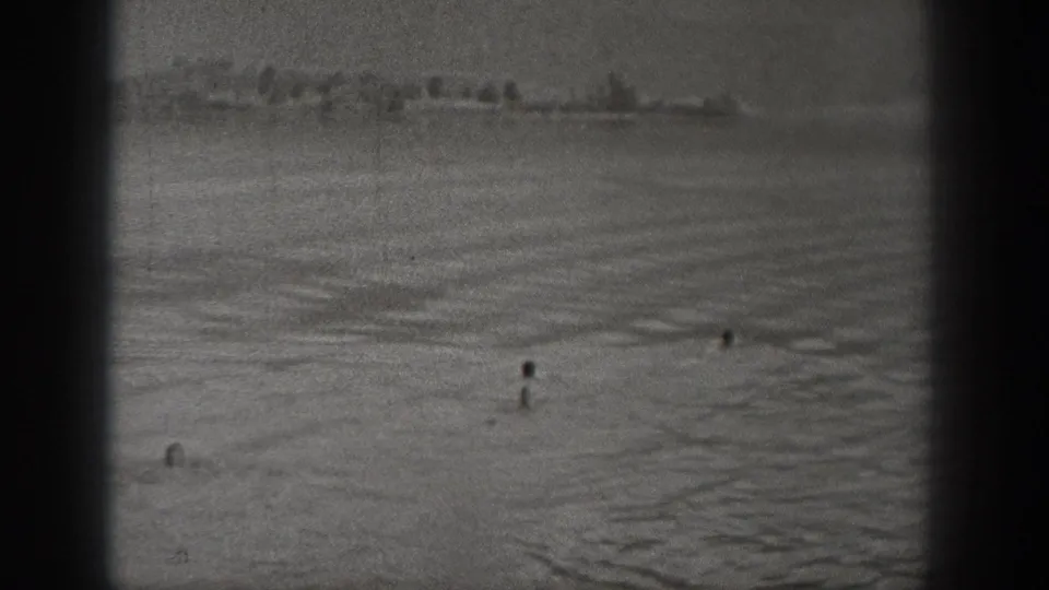 Black-and-white 8mm frame of open Washington water with several distant people and shoreline detail.