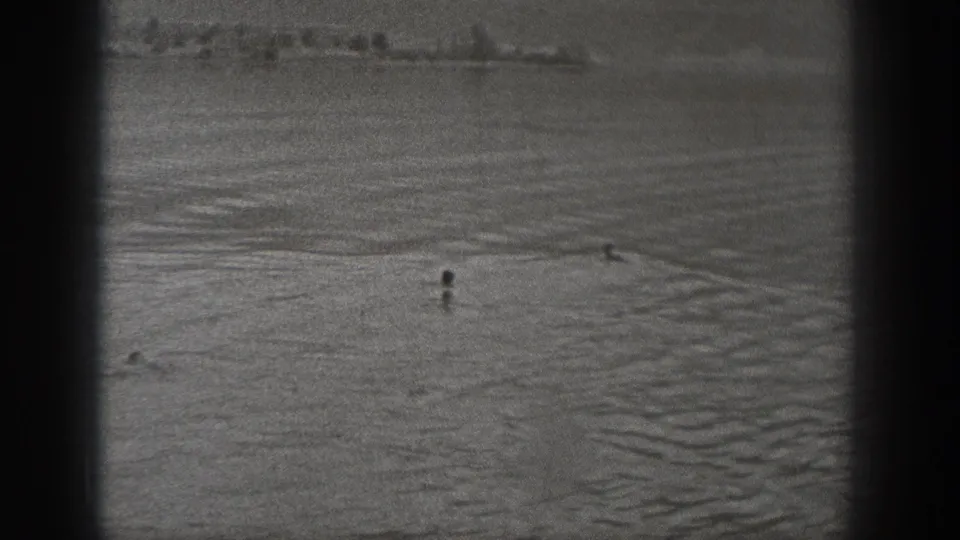 1940 Washington waterfront frame with distant people in the water and a small craft or object farther across the surface.