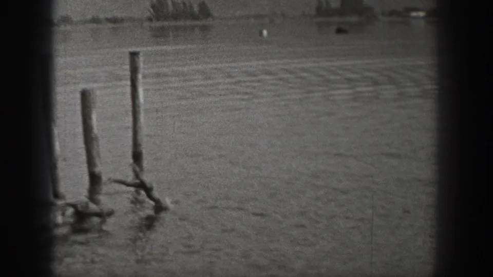 1940 Washington home-movie frame showing wooden posts near the camera, open water, and faint shoreline beyond.