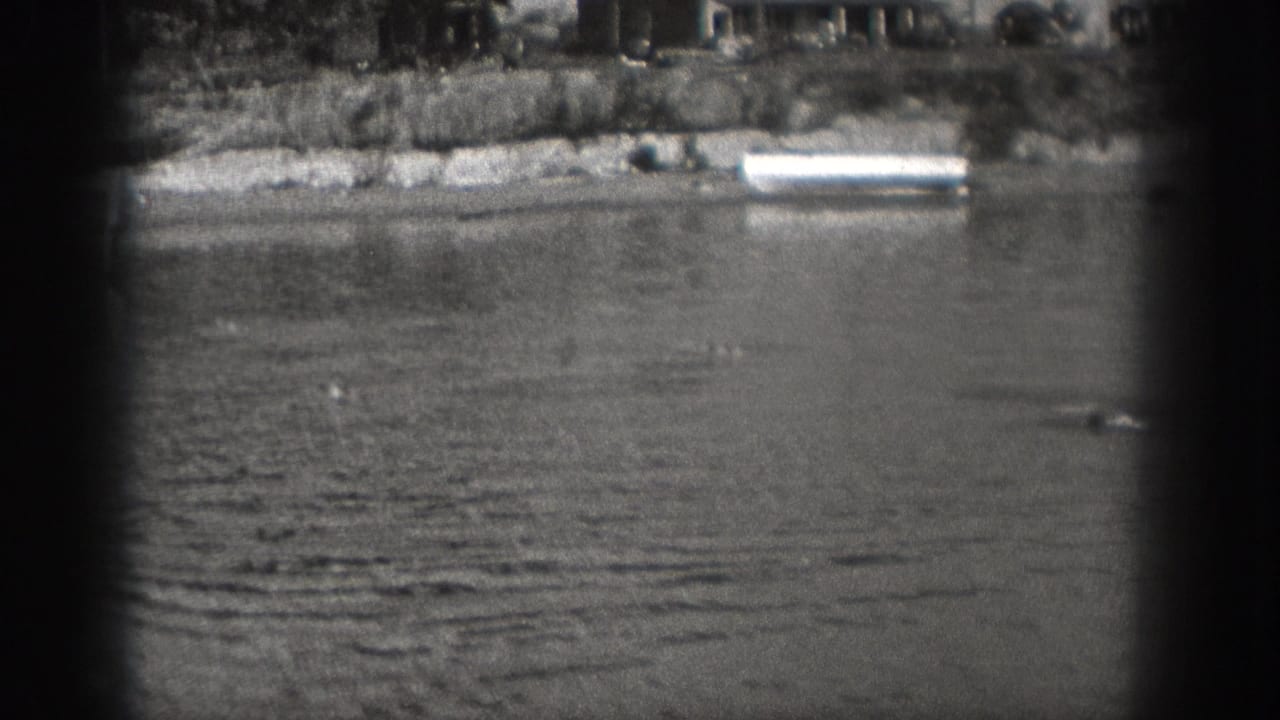 Washington 1940 home-movie frame showing a calm river, distant shoreline, and dark vignetted 8mm frame edges before the boat enters clearly.