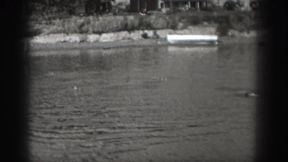 Washington 1940 home-movie frame showing a calm river, distant shoreline, and dark vignetted 8mm frame edges before the boat enters clearly.