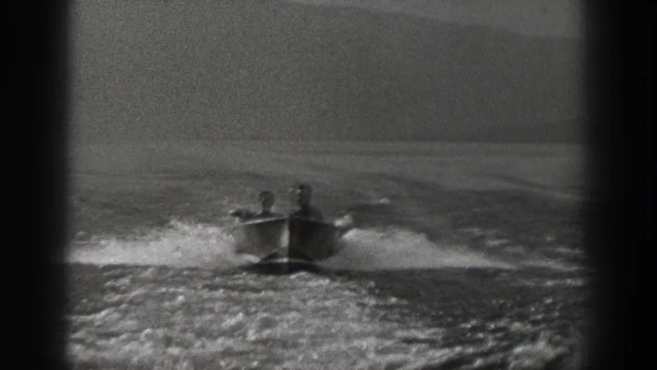 Two adult men ride in a small motorboat on a Washington river in 1940, with spray and wake spreading behind the boat.