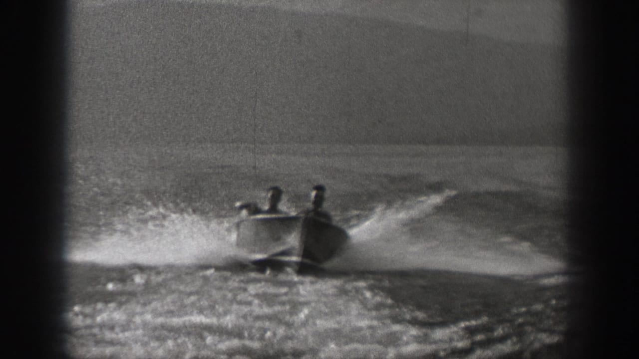 Two young men ride in a small motorboat on open water in Washington, 1940, with spray and wake behind them.