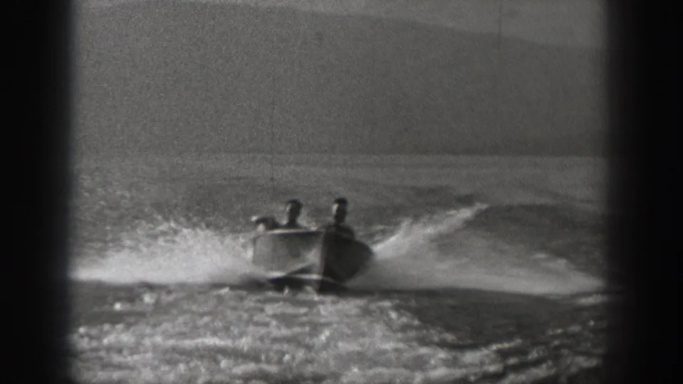 Two young men ride in a small motorboat on open water in Washington, 1940, with spray and wake behind them.