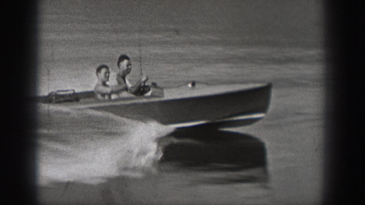 A small motorboat with two riders moves across the lake while spray rises near the hull.
