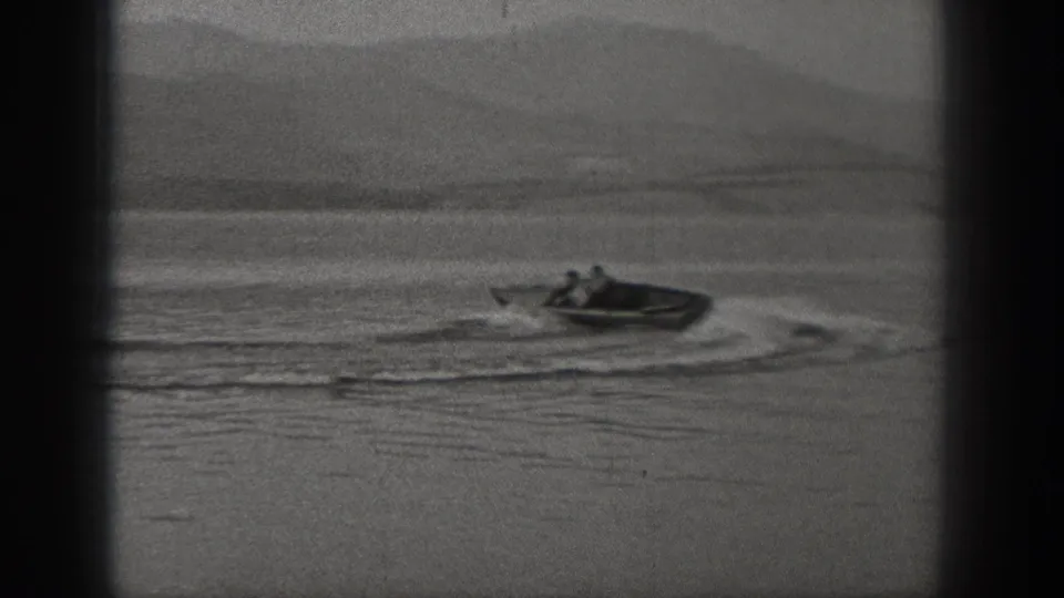 Black-and-white Washington lake scene with a small motorboat at distance, circular wake lines, and faint mountain forms in the background.