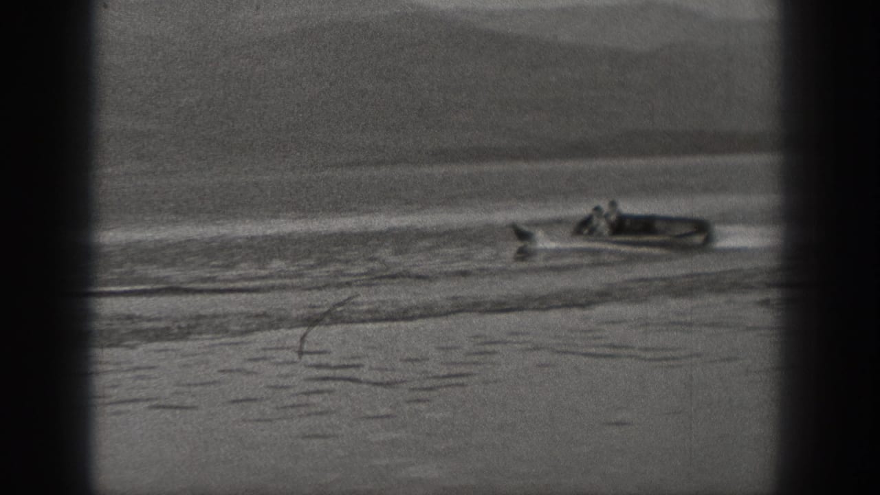 1940 Washington 8mm frame showing two people in a small motorboat crossing calm lake water with a wake behind them.