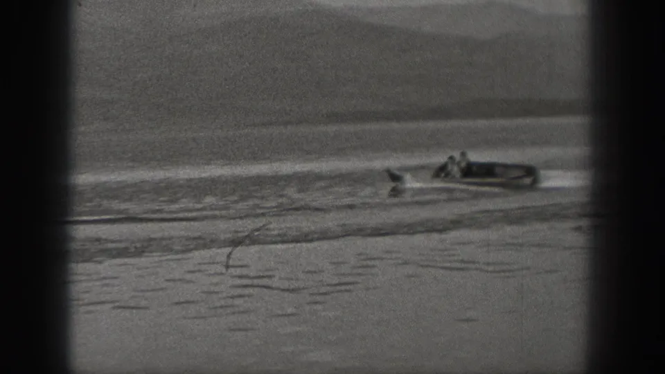 1940 Washington 8mm frame showing two people in a small motorboat crossing calm lake water with a wake behind them.