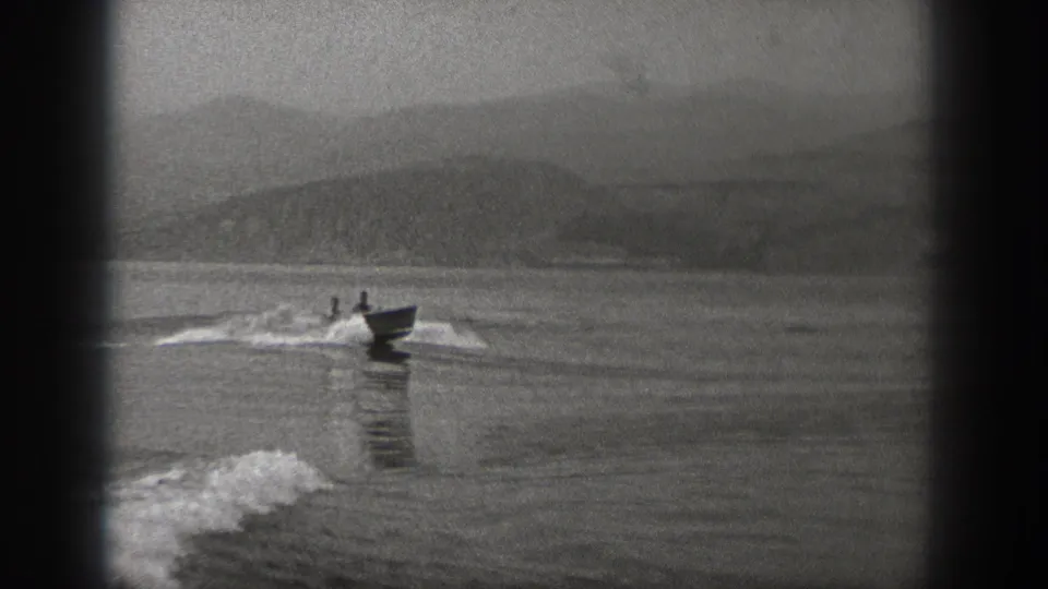 Two people in a small motorboat approach across a calm Washington lake with distant mountains behind them.