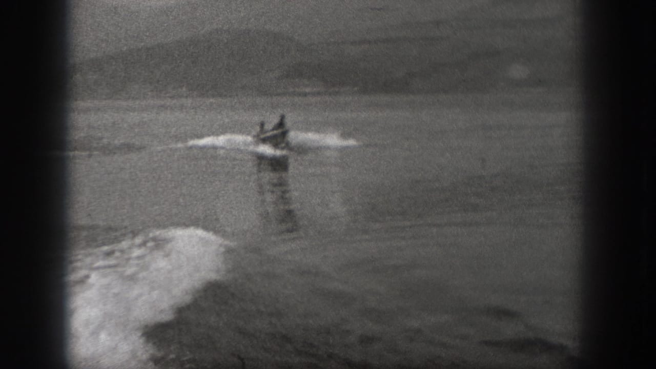 Motorboat farther across the water with two figures aboard and wake spreading behind it.
