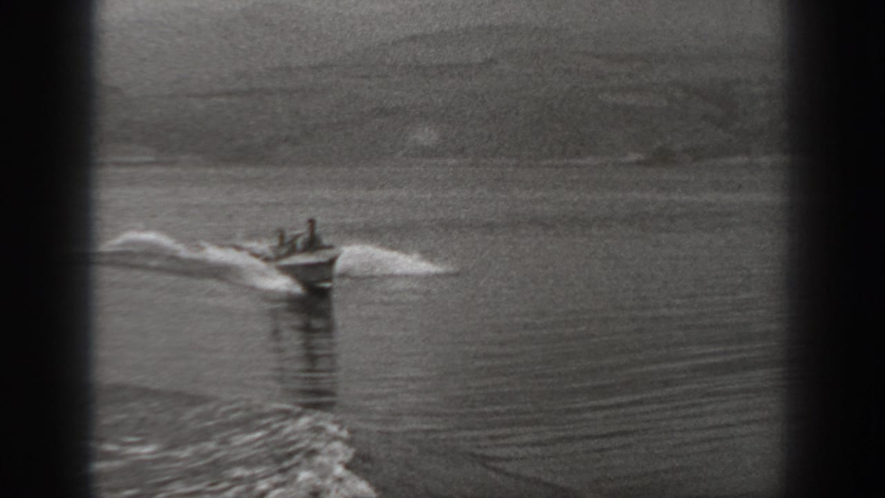 1940 Washington home-movie frame showing two people in a small motorboat crossing calm water with a white wake behind them.
