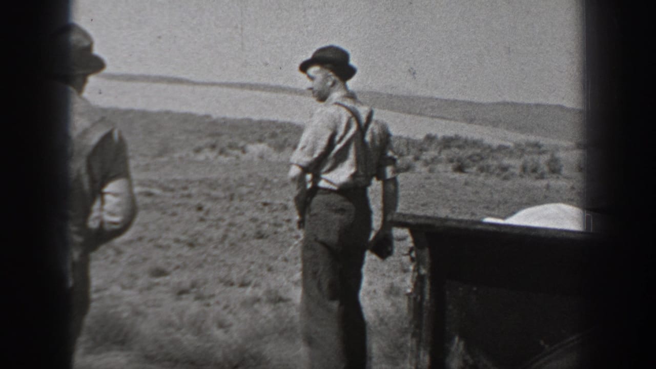 Black-and-white 1940 Washington home-movie frame showing adult men in hats near a vintage car in open desert terrain.