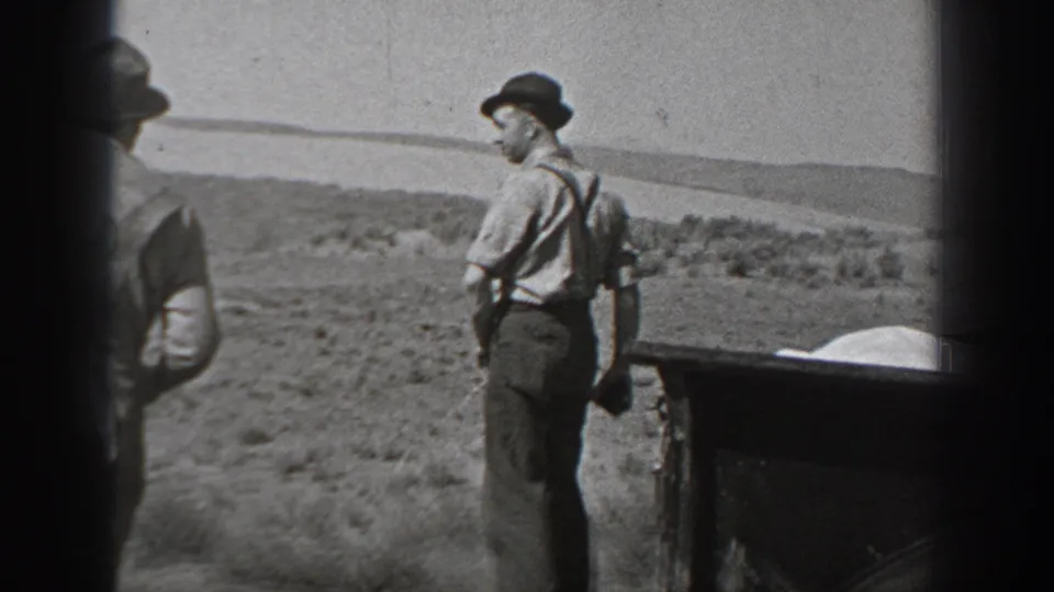 Black-and-white 1940 Washington home-movie frame showing adult men in hats near a vintage car in open desert terrain.