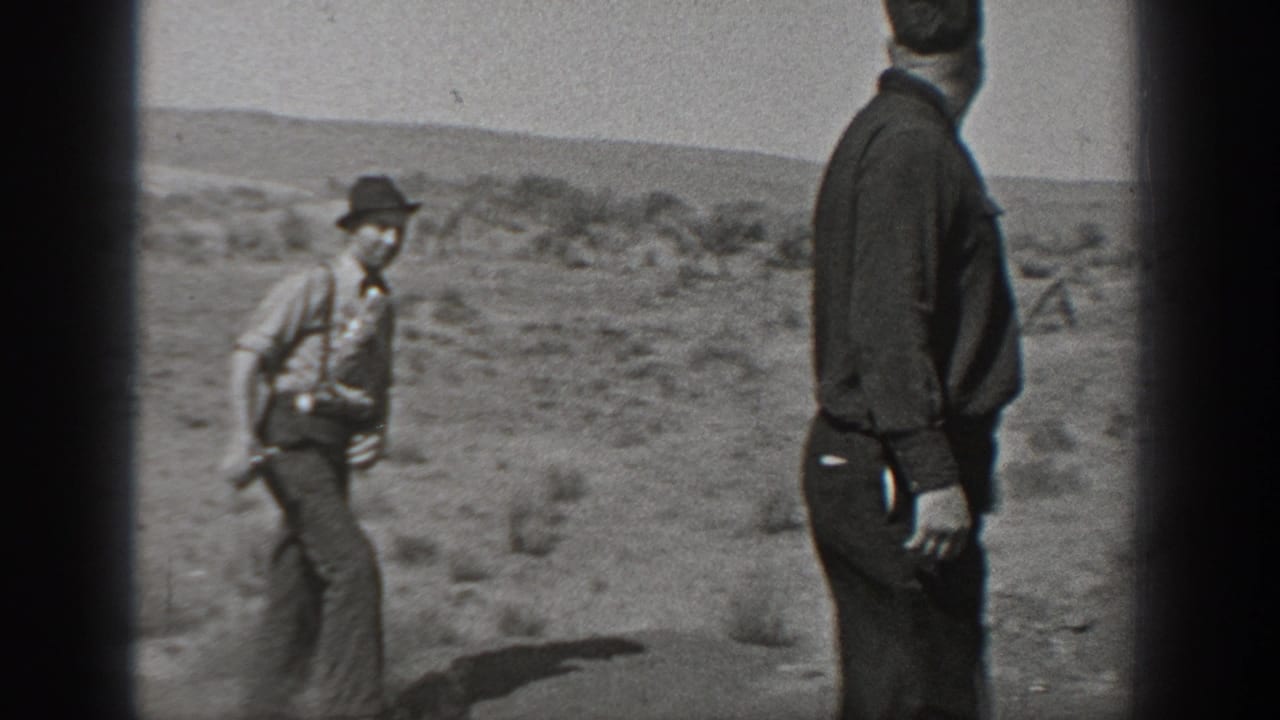 Two men stand and walk in a dry roadside landscape.