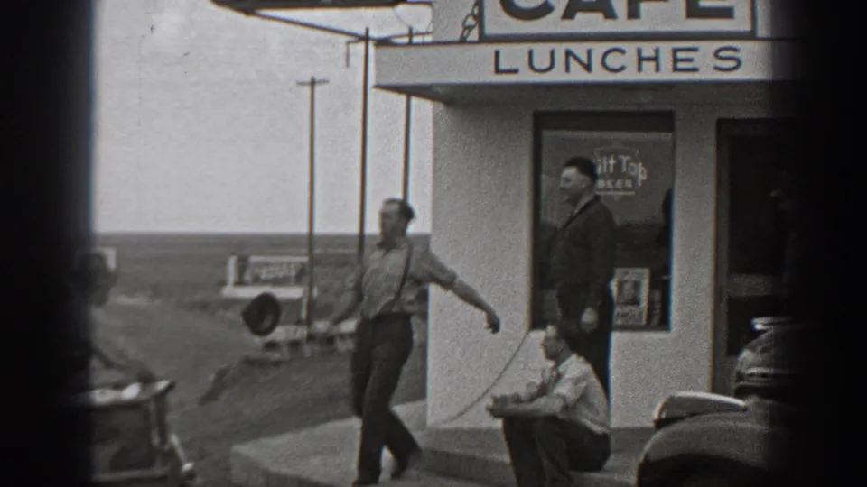 1940 Washington home-movie frame showing men around Fred's Cafe steps, a parked car, and the LUNCHES sign above.