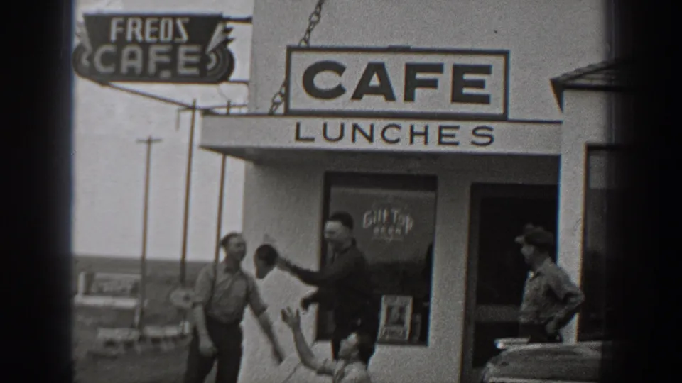 1940 Washington home-movie frame showing men joking near Fred's Cafe while a hat is passed outside the entrance.