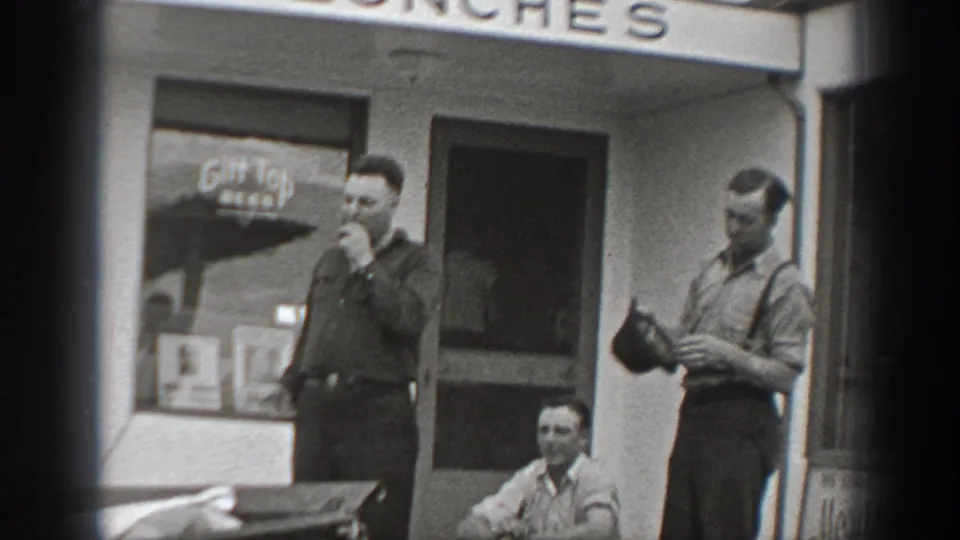 Men in period work clothes gather outside a Washington cafe, with a beer sign visible in the window.