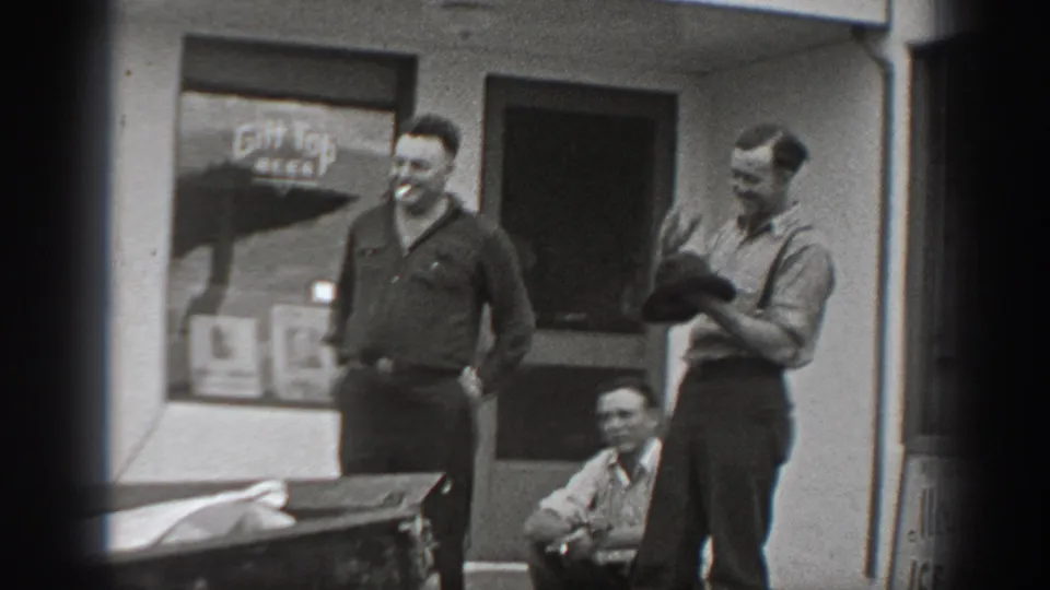A brief home-movie moment of men socializing outside a Washington cafe, with signage and workwear visible.