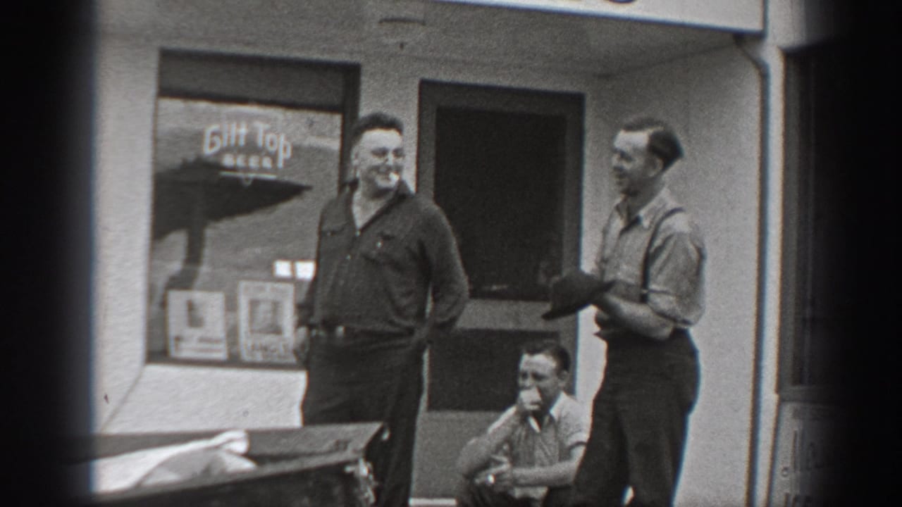 Three adult men outside a storefront, with one seated on the stoop and a Gilt Top Beer sign in the window.