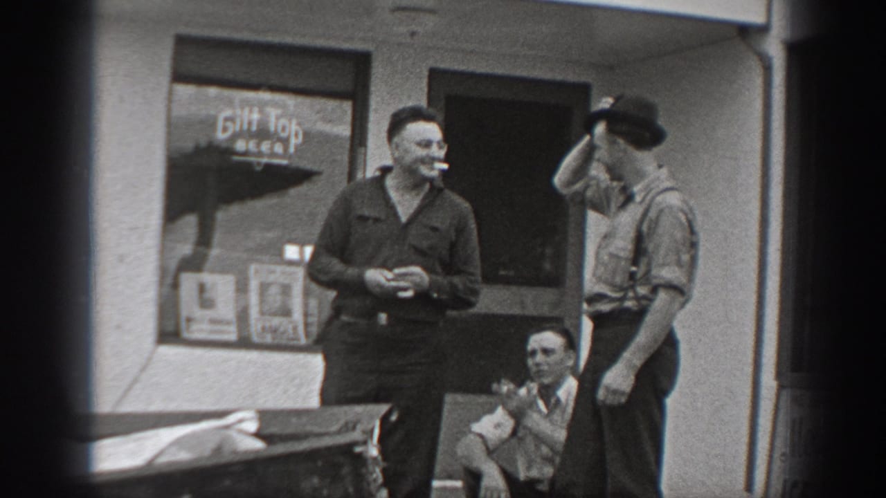 Two men stand outside the storefront while another sits near the doorway and a beer sign appears in the window.