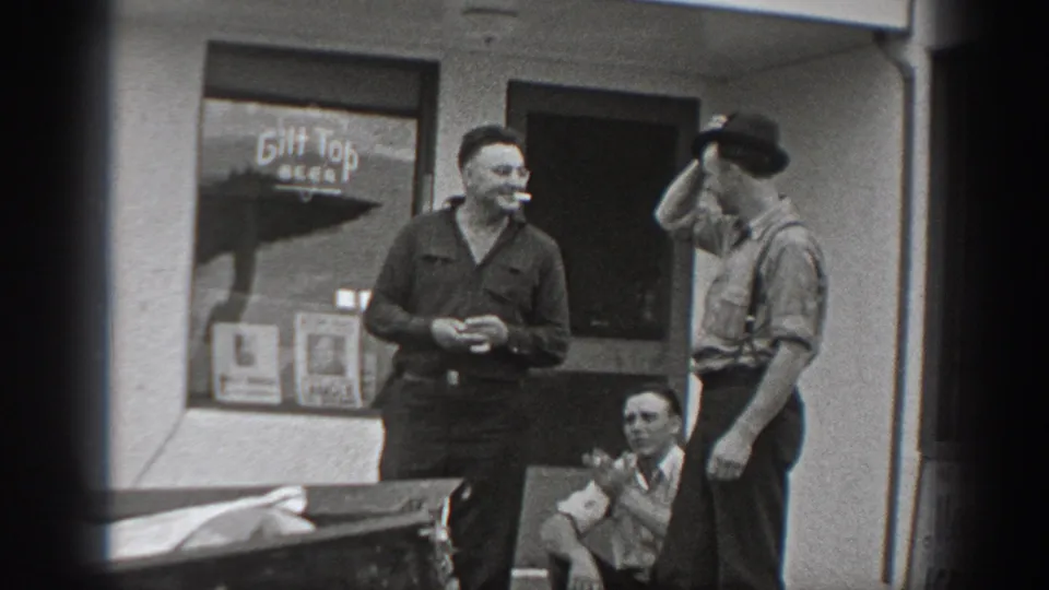 1940 Washington frame of adult men outside a shopfront, including a smoker and a man holding a hat near a visible Gilt Top Beer window sign.